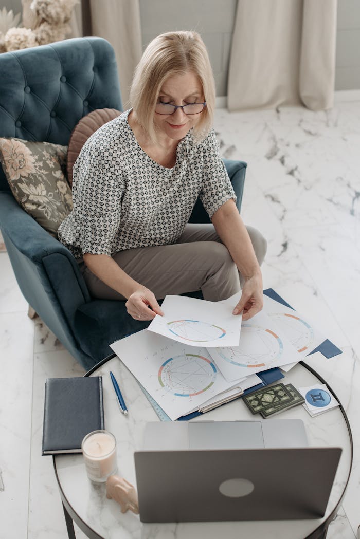 Elderly woman examines astrology charts on a laptop in a cozy living room setting.