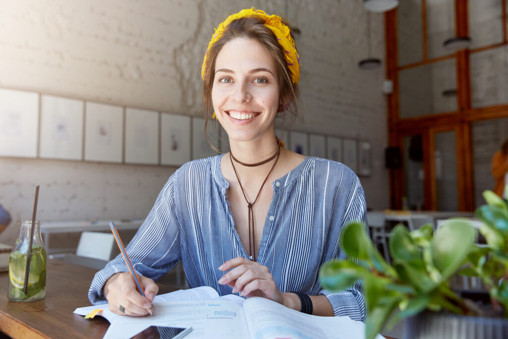 young woman wearing bandana studying cafe 1 - „Wspieramy każdego w odkrywaniu i rozwijaniu swojego potencjału, by żyć pełnią życia”